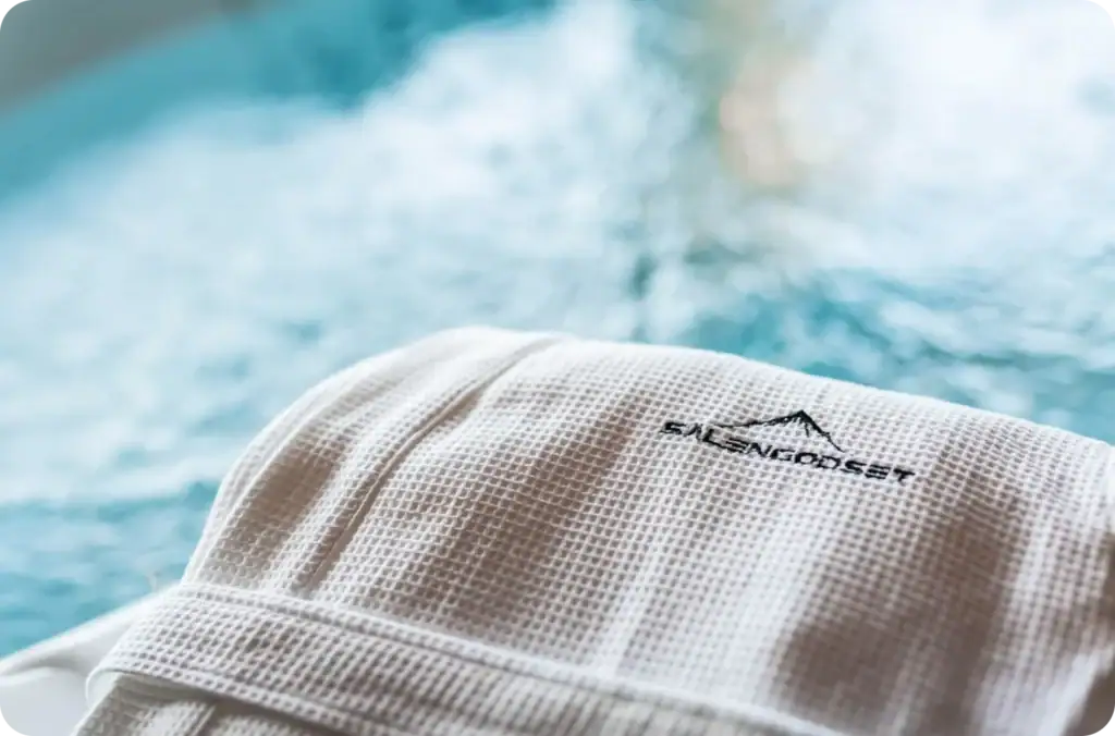 Vit badrock med Sälengodsets logotyp vid bubbelpool i fjällstuga.