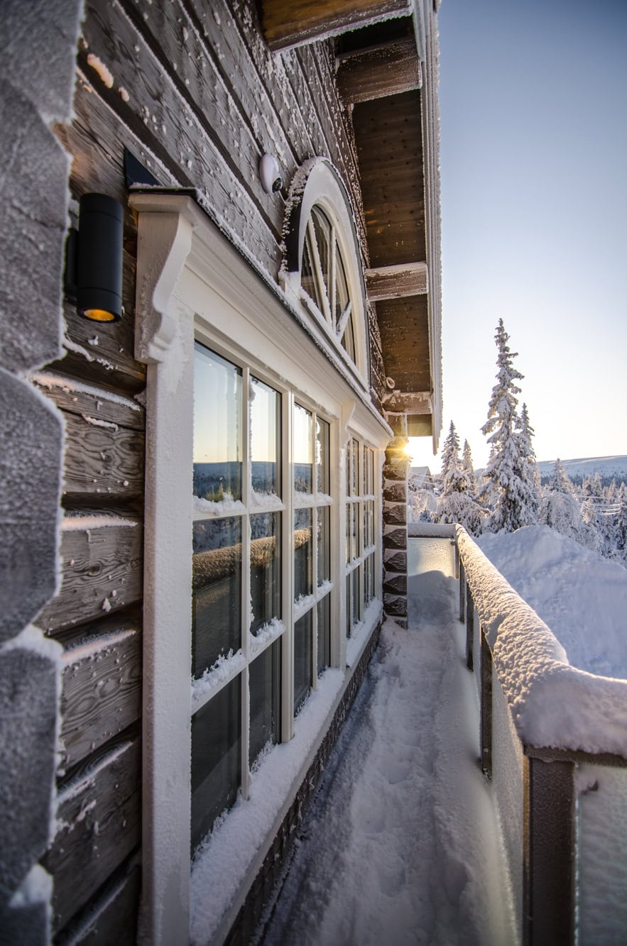 Husvägg med snötäckta fönster och klassisk träfasad i vinterskymning.