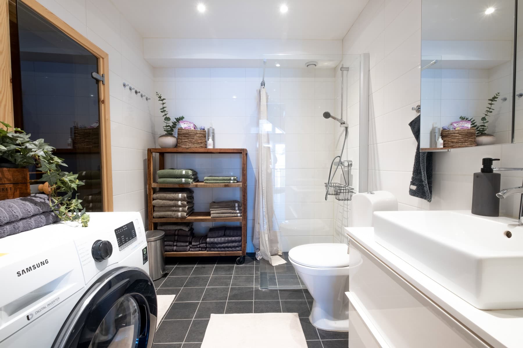 Renovert badrum med modern design, tvättmaskin och praktiska förvaringslösningar för badrumsartiklar. ljusa väggar och mörkgrå golv skapar en stilren och funktionell atmosfär för optima.