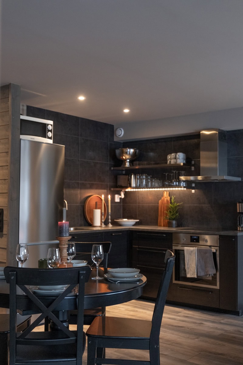 Modern svart köksinredning med matbord och stämningsfull belysning för en behaglig matsalsmiljö.