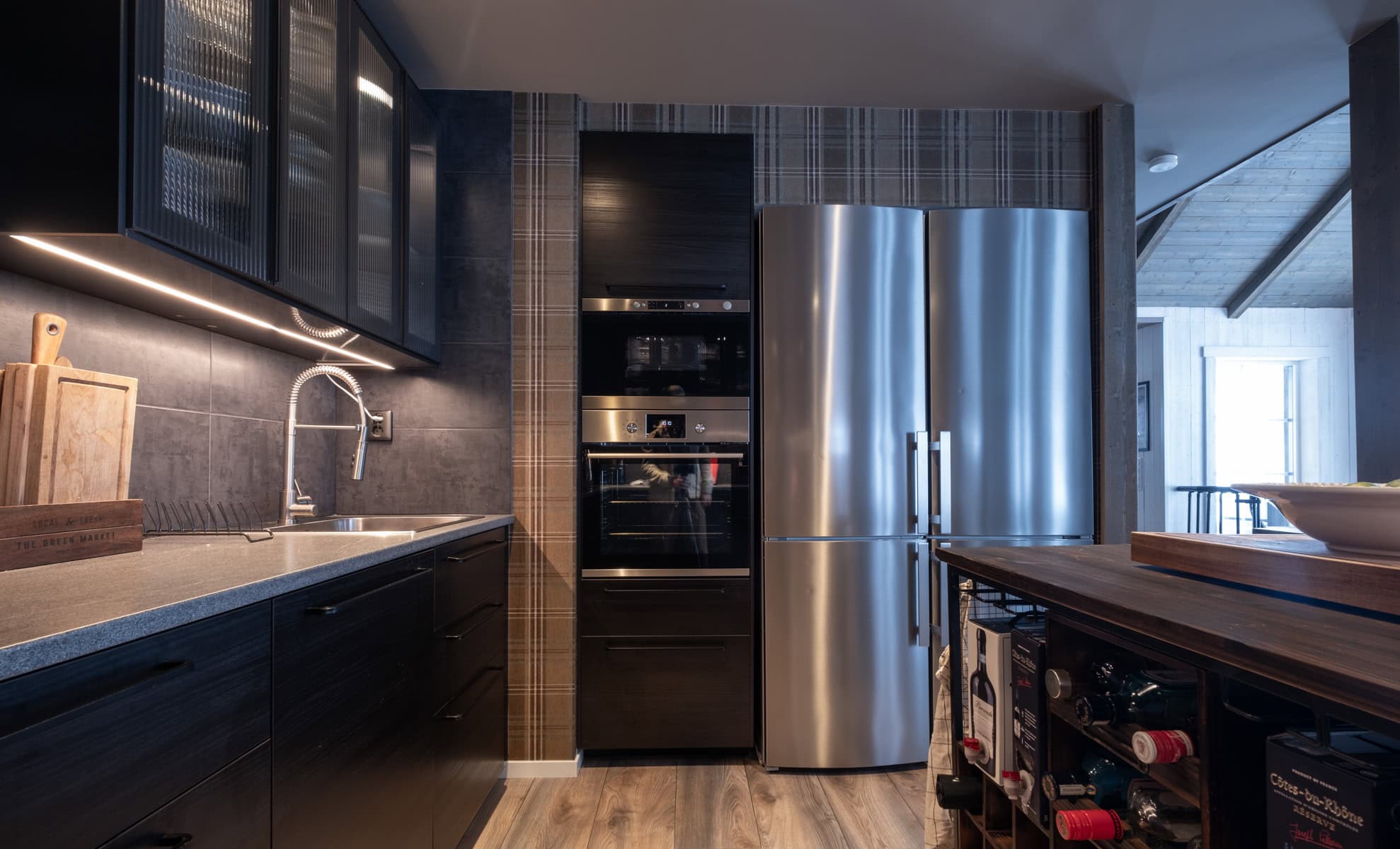 Modern kök med rostfria kylskåp, svarta skåpluckor, grå bänkskiva och rustik trädetalj i en stilfull bostadsmiljö.