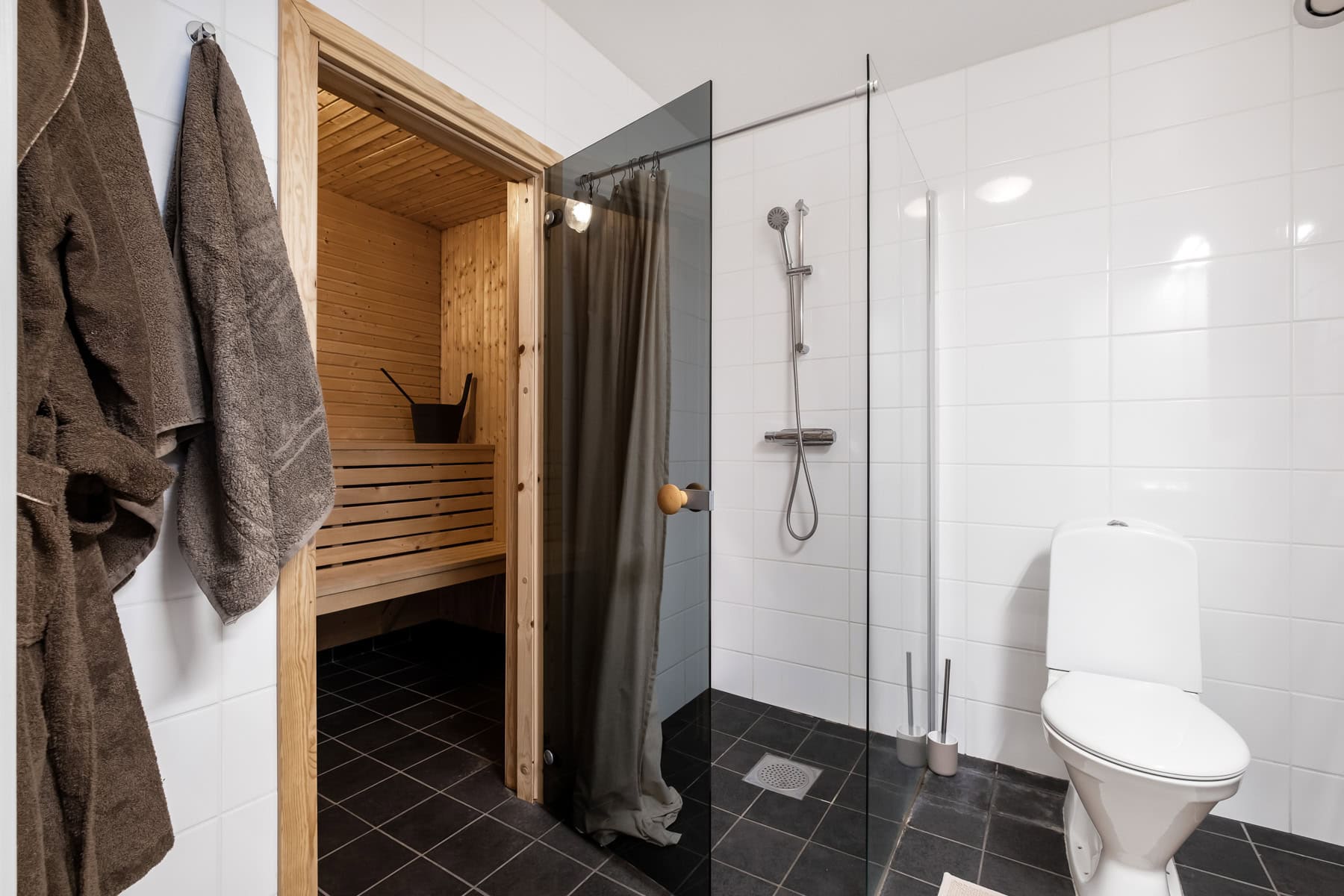 Modern badrum med bastu, dusch och toalett, inrett med svart kakel och vita väggar för en avkopplande spa-känsla. Perfekt för avkoppling och wellness hemma eller på fritidsboende.