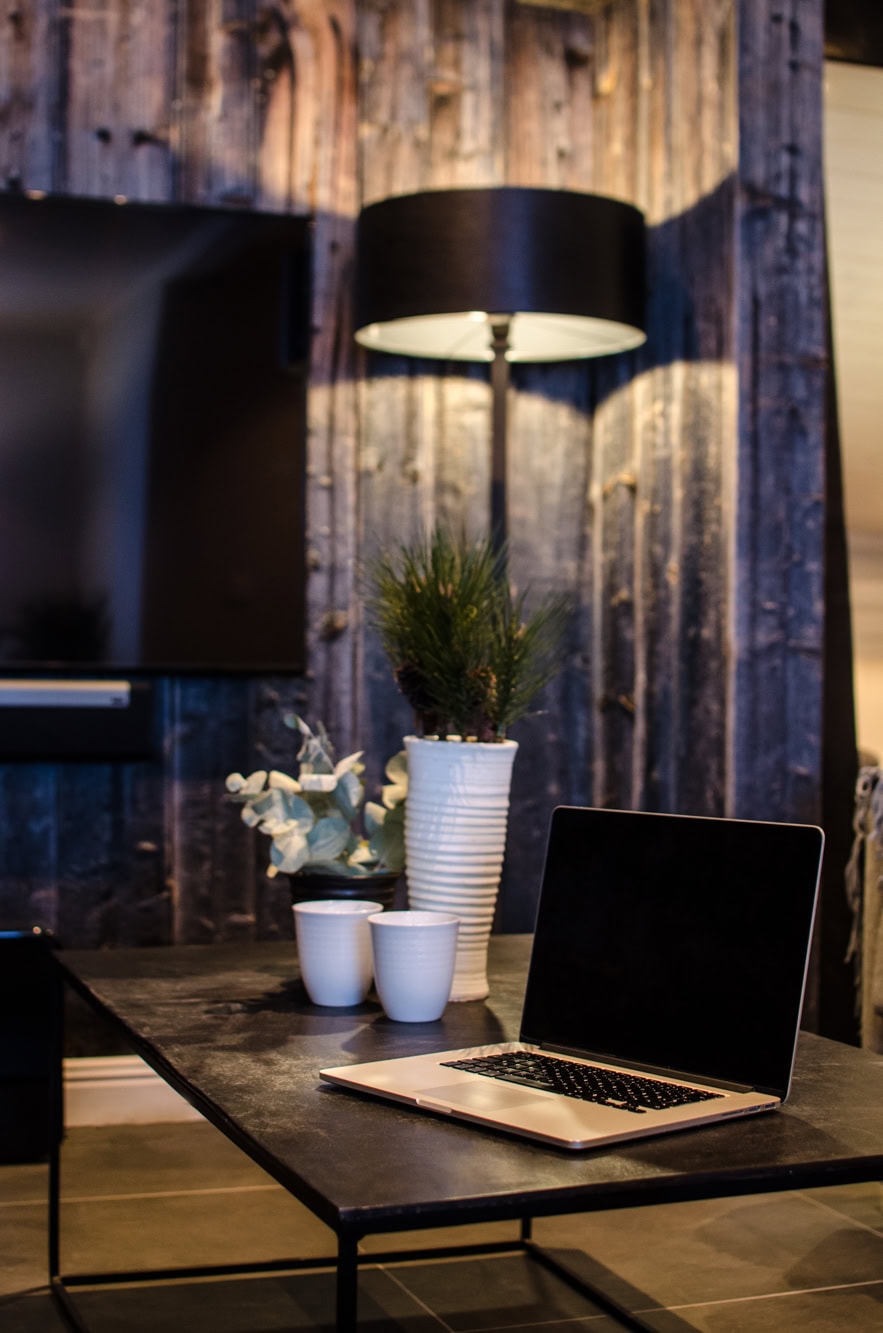 Laptop på svart bord i en modern inredningsstil med växt och ljus, rustik backgroun av trävägg, skapar en mysig och inspirerande arbetsmiljö.