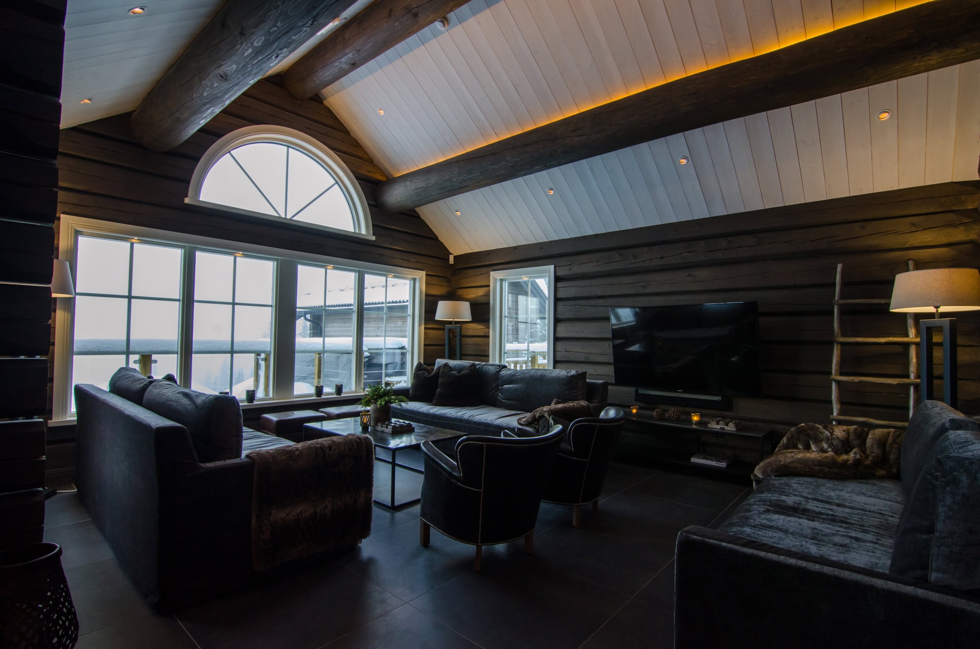 Ljus och modern salong med stora fönster, träväggar och lyxiga soffor, perfekt för avkoppling och sociala tillfällen.