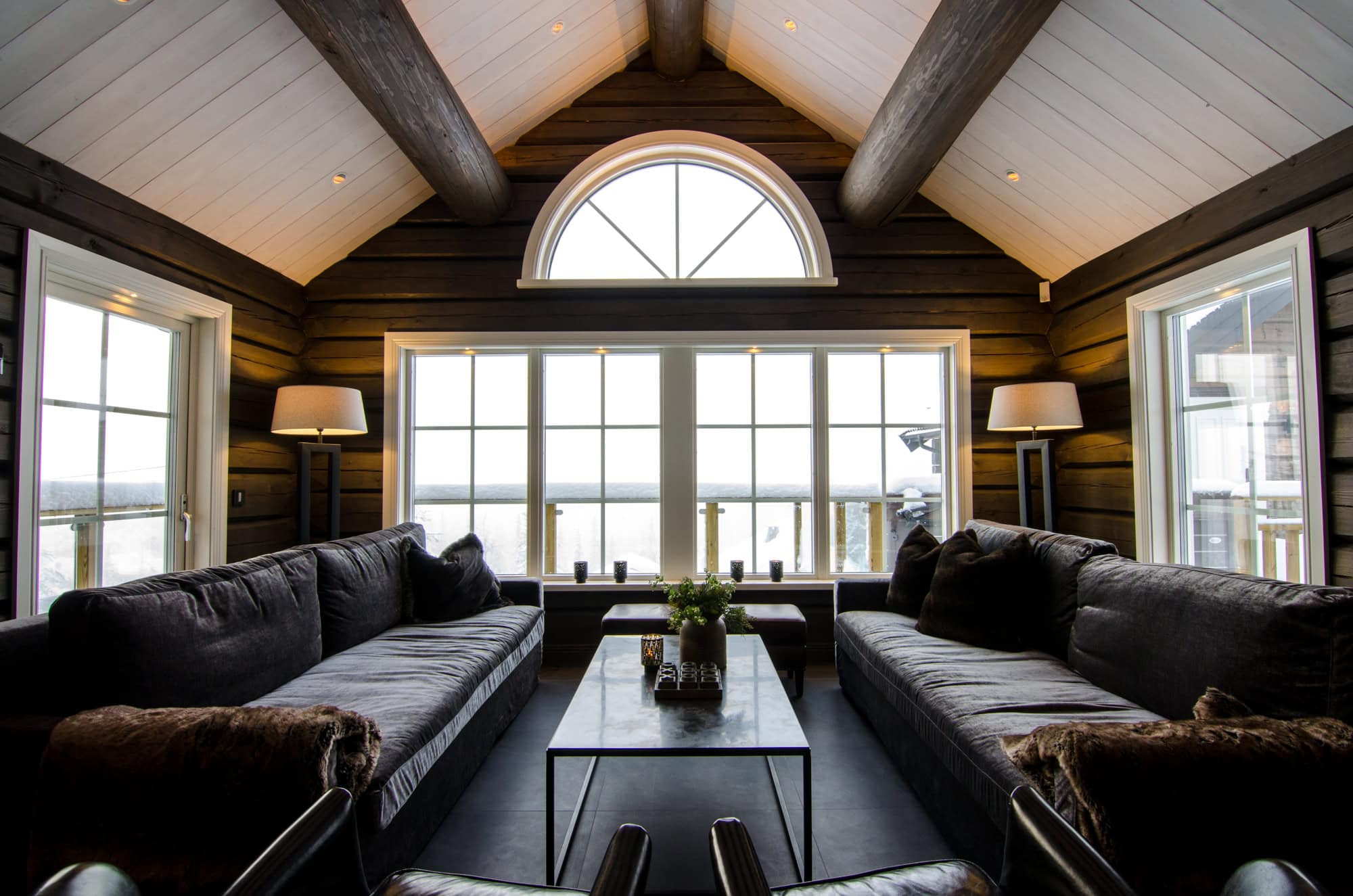 Elegant rustikhus inredning med stora fönster, träväggar och bekväma soffor, perfekt för avkoppling i natursköna miljöer, idealiskt för salong och avkoppling i naturnära boende.
