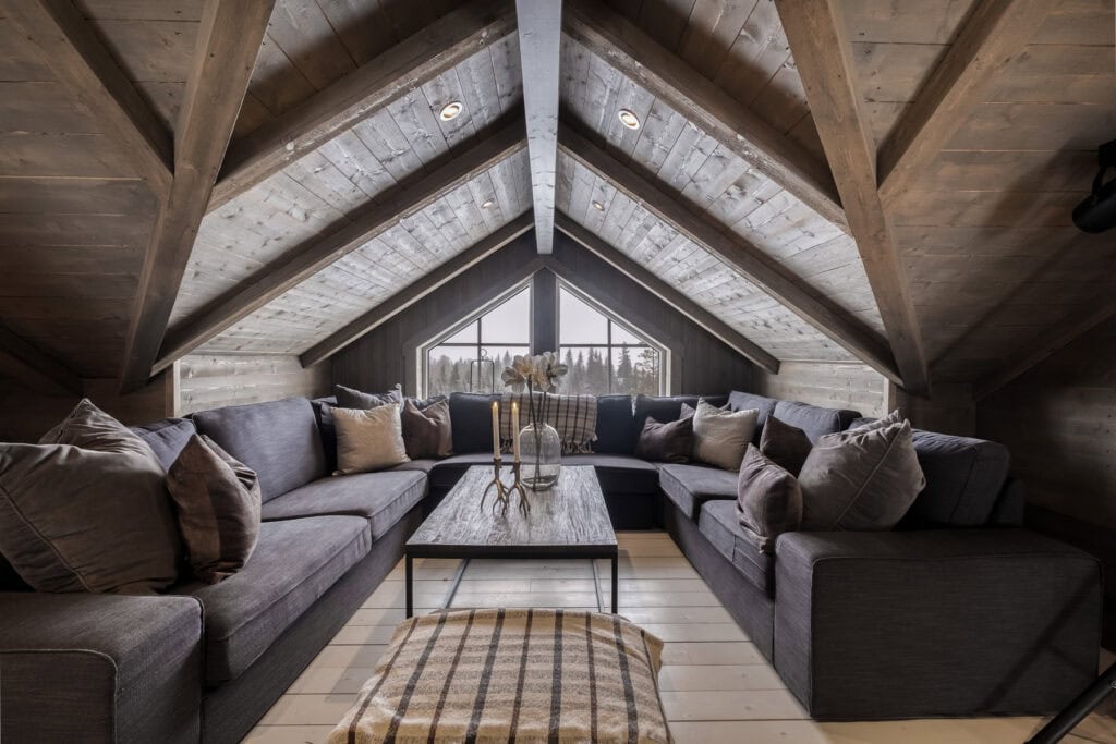 Mysig loftlounge med stora soffor och utsikt över fjällskog i Sälen