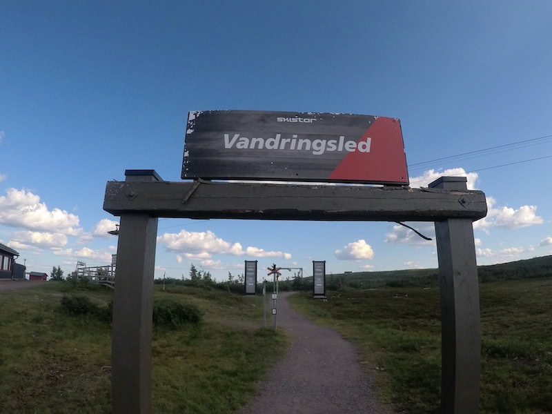 Skylt vid starten av en vandringsled i Sälenfjällen en solig sommardag, med blå himmel och grusväg som leder ut på fjället.