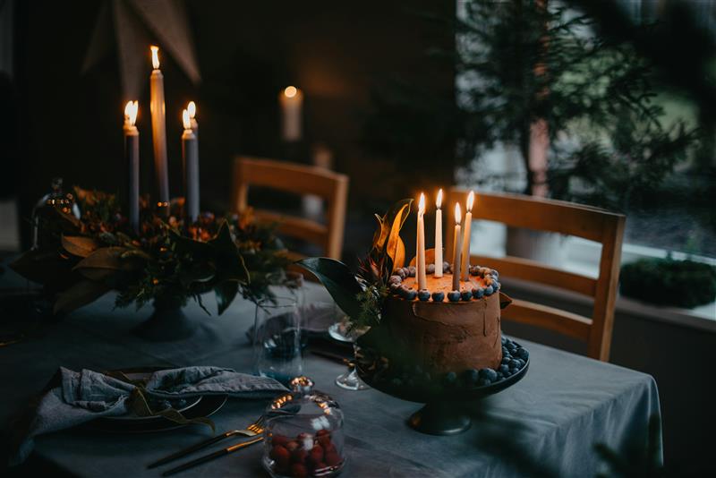 Gâteau d'anniversaire avec bougies allumées et baies sur une table dressée dans un refuge de montagne.