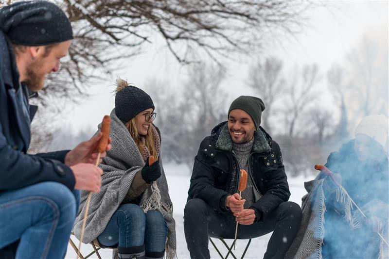 Vänner grillar korv tillsammans över öppen eld i vintrigt landskap