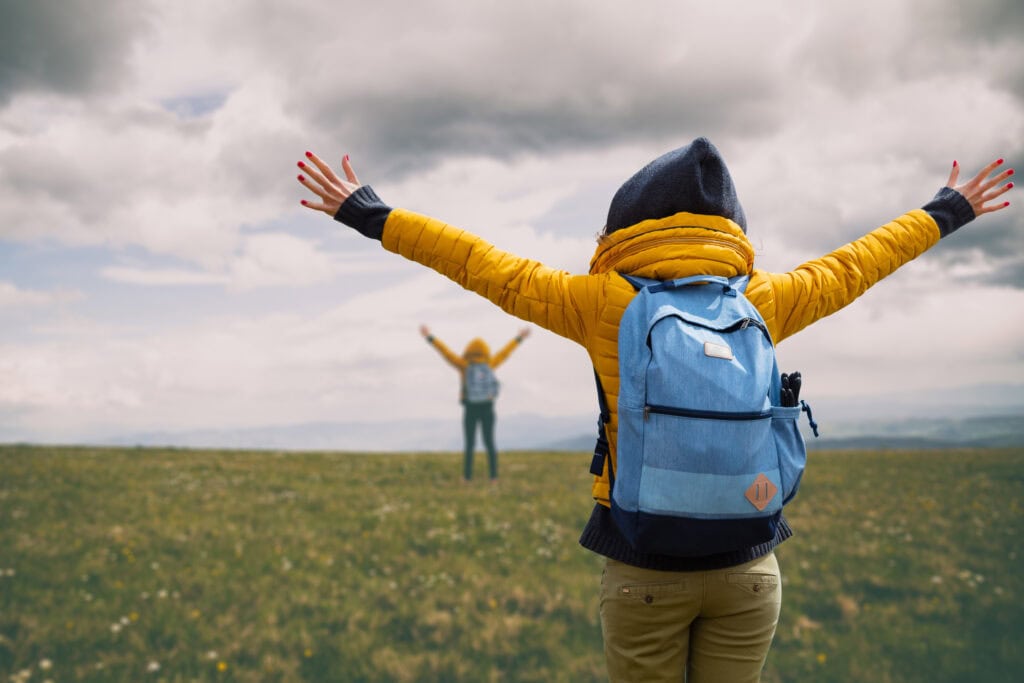Vandrare med ryggsäck sträcker ut armarna över en fjälläng i Sälen