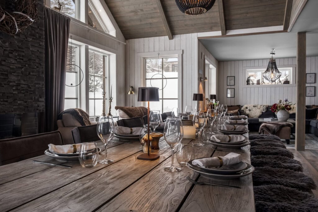 Ljust inredd matsal i lantlig stil med rustik träbord, moderna belysningar och stora fönster med utsikt över snötäckta landskap. Perfekt för middagar och sociala tillställningar i ett mysigt hem.