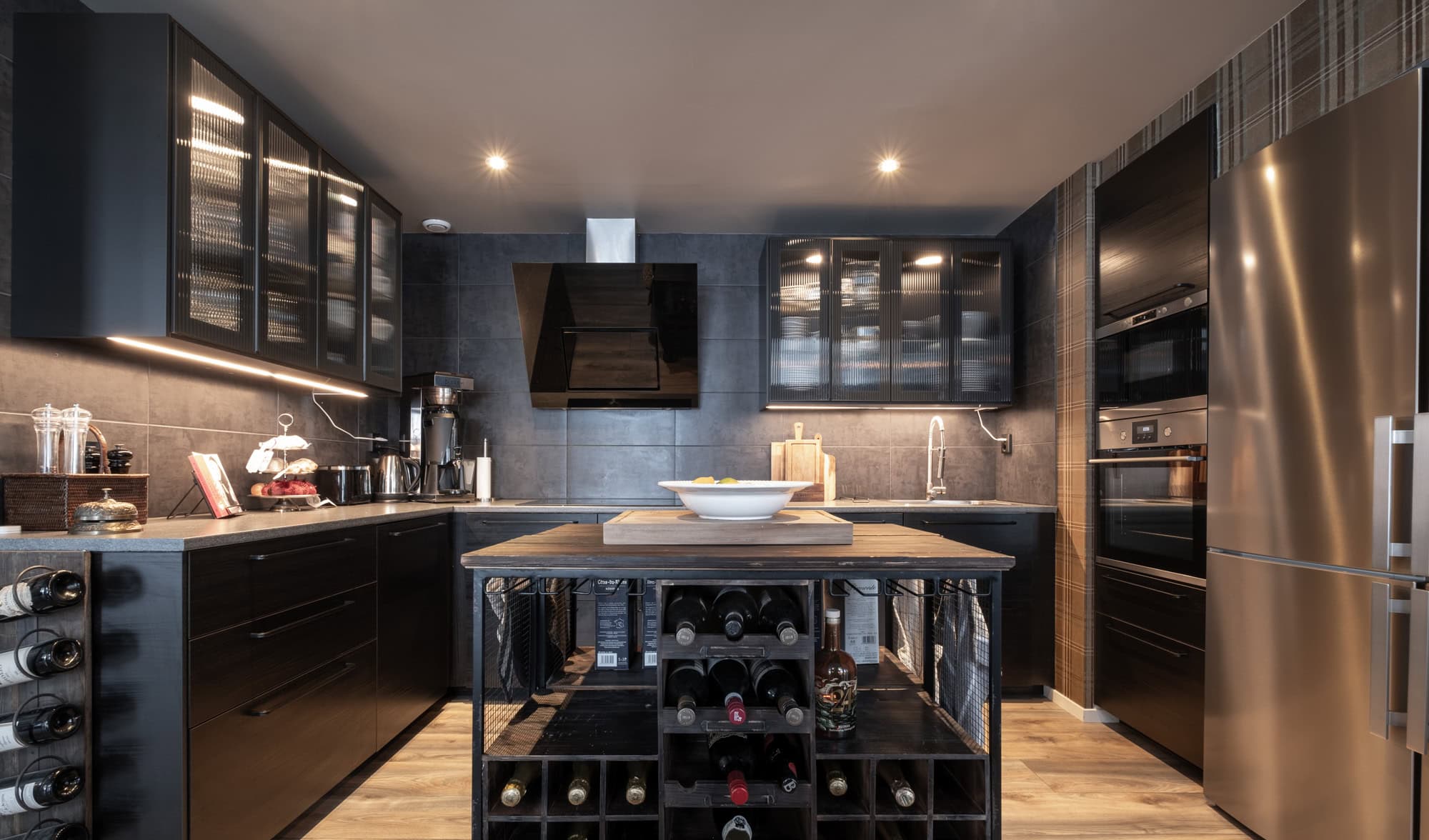 Modern svart och rostfritt kök med inbyggda apparater, vinförvaring och stilren belysning – perfekt för en elegant och funktionell måltidsupplevelse.