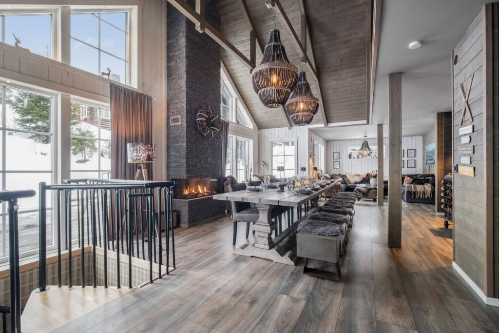 Rustikvinterinredning med öppen planlösning, stora fönster, braskamin och elegant matplats i trä, perfekt för mysiga tillställningar; speglar och naturliga material för en varm, inbjudande atmosfär.