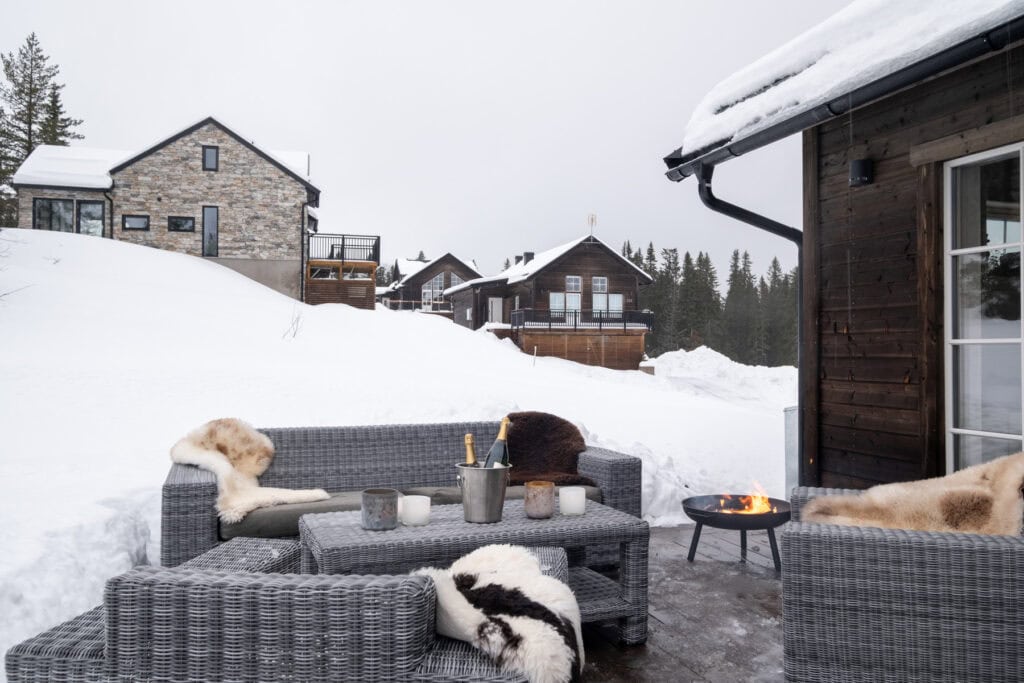 Lichte en uitnodigende eethoek buiten met zitmeubilair, om op te warmen bij een vuurkorf in een besneeuwde alpine omgeving, omringd door bos en gezellige chalets, perfect om te ontspannen in de winter.