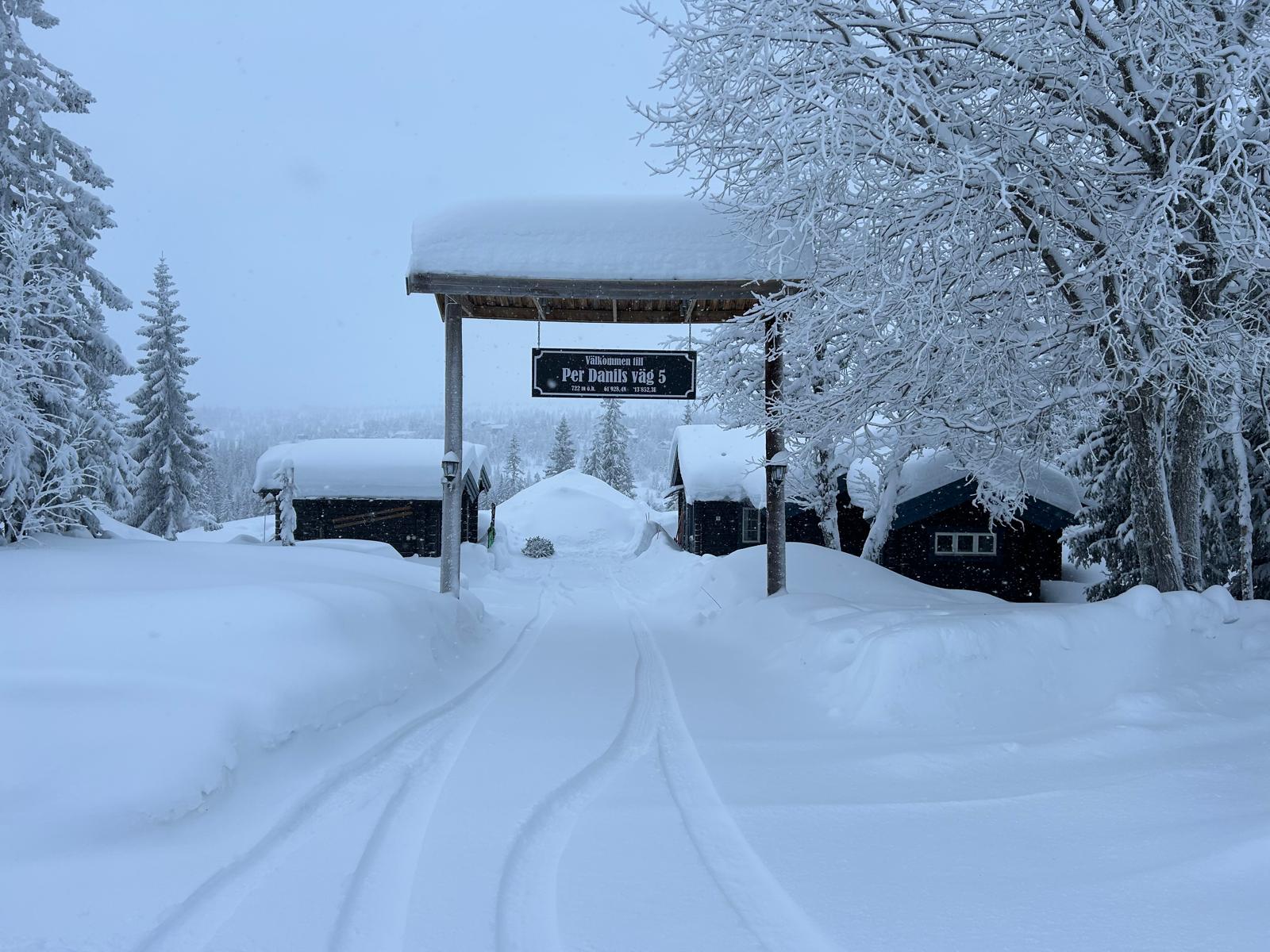 Snöigt landskap med stugor och skylt.