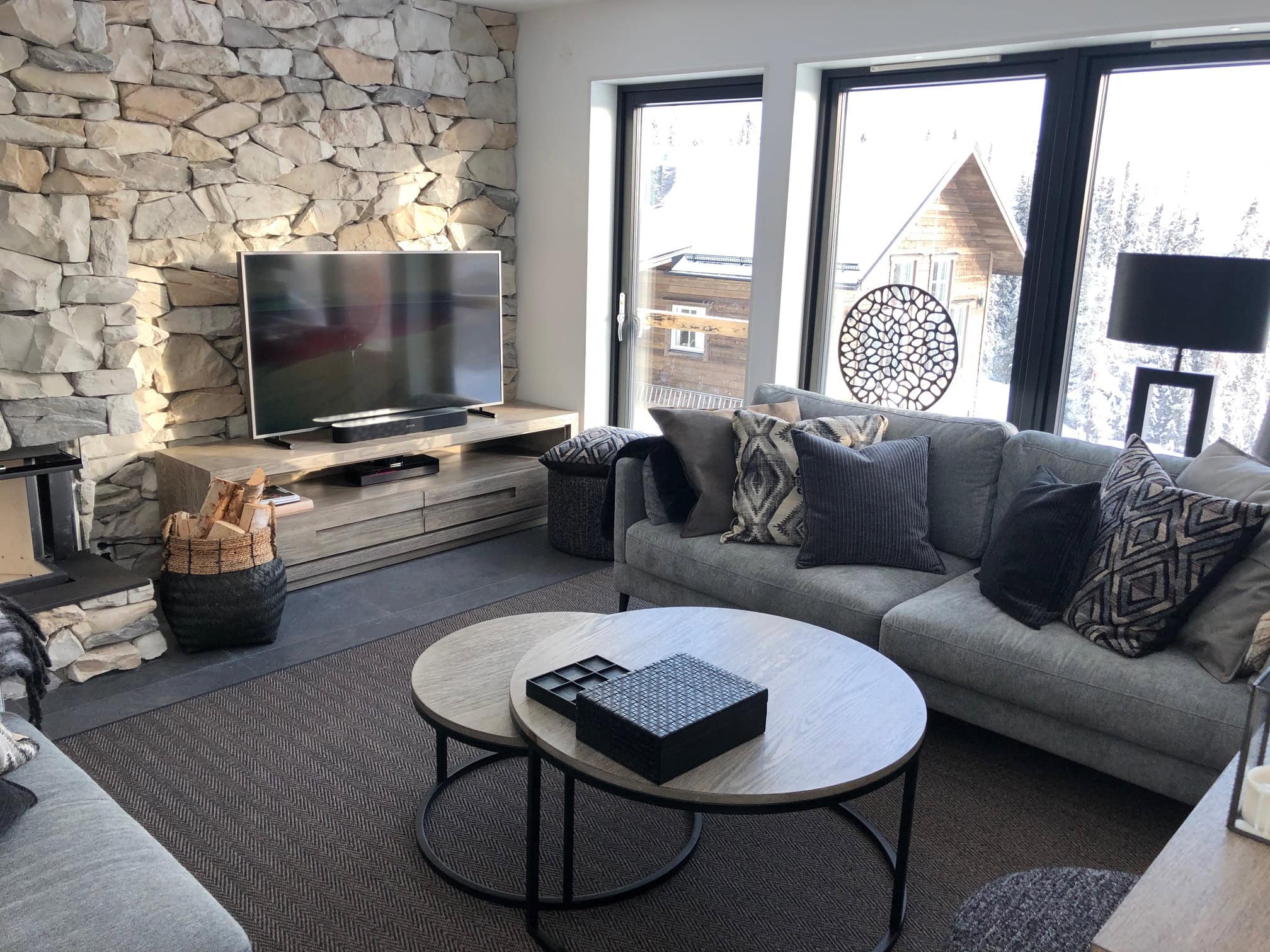 Modernes Wohnzimmer mit großem Sofa, Fernseher und großen Fenstern mit Blick auf die verschneite Landschaft.