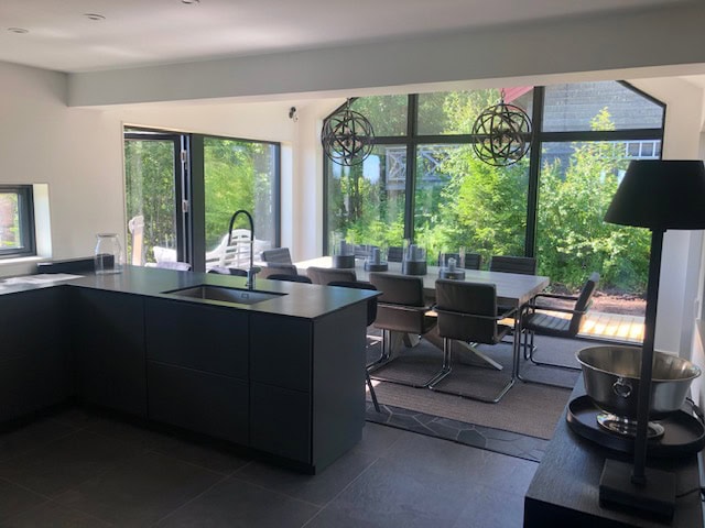 Elegante Küche und Esszimmer mit großen Fenstern, die viel Tageslicht hereinlassen, modernen Möbeln und Blick auf grüne Bäume.