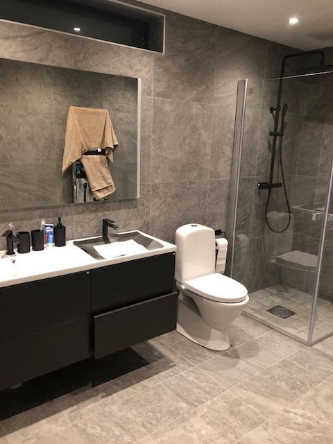 Modernes Badezimmer mit Dusche, Toilette, schwarzem Waschbeckenschrank, Spiegel und grauen Wänden für einen stilvollen Look.