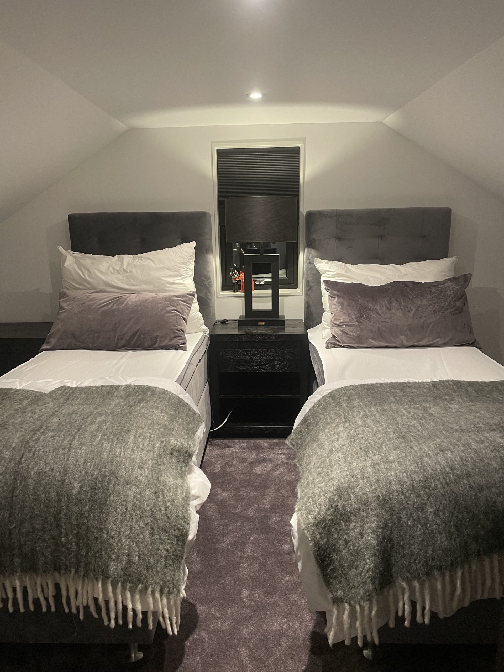 Modernes Schlafzimmer mit zwei Betten, dunklen Nachttischen und einem Spiegel, heller Wand- und Deckenbeleuchtung sowie eleganter Einrichtung.