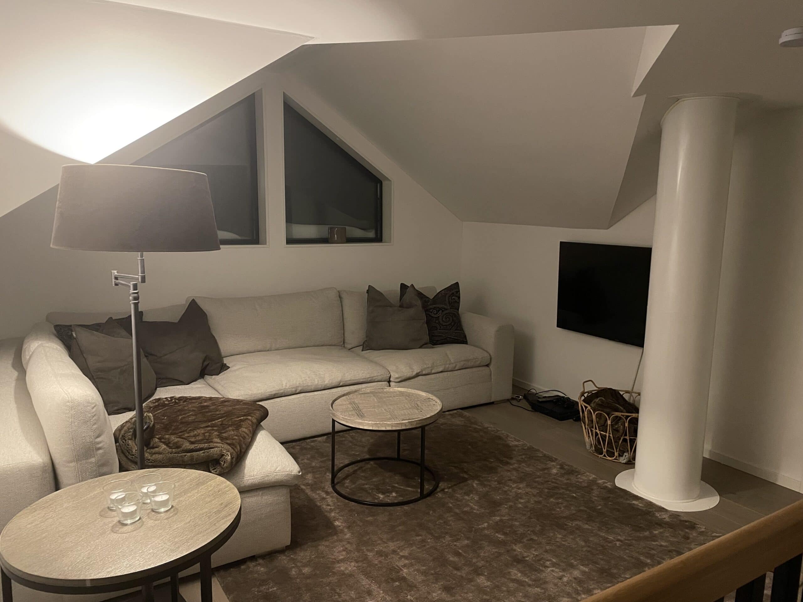Wohnzimmer mit hellem Sofa, rundem Couchtisch und an der Wand montiertem Fernseher in einem modernen Zuhause mit Dachfenstern und minimalistischer Einrichtung.