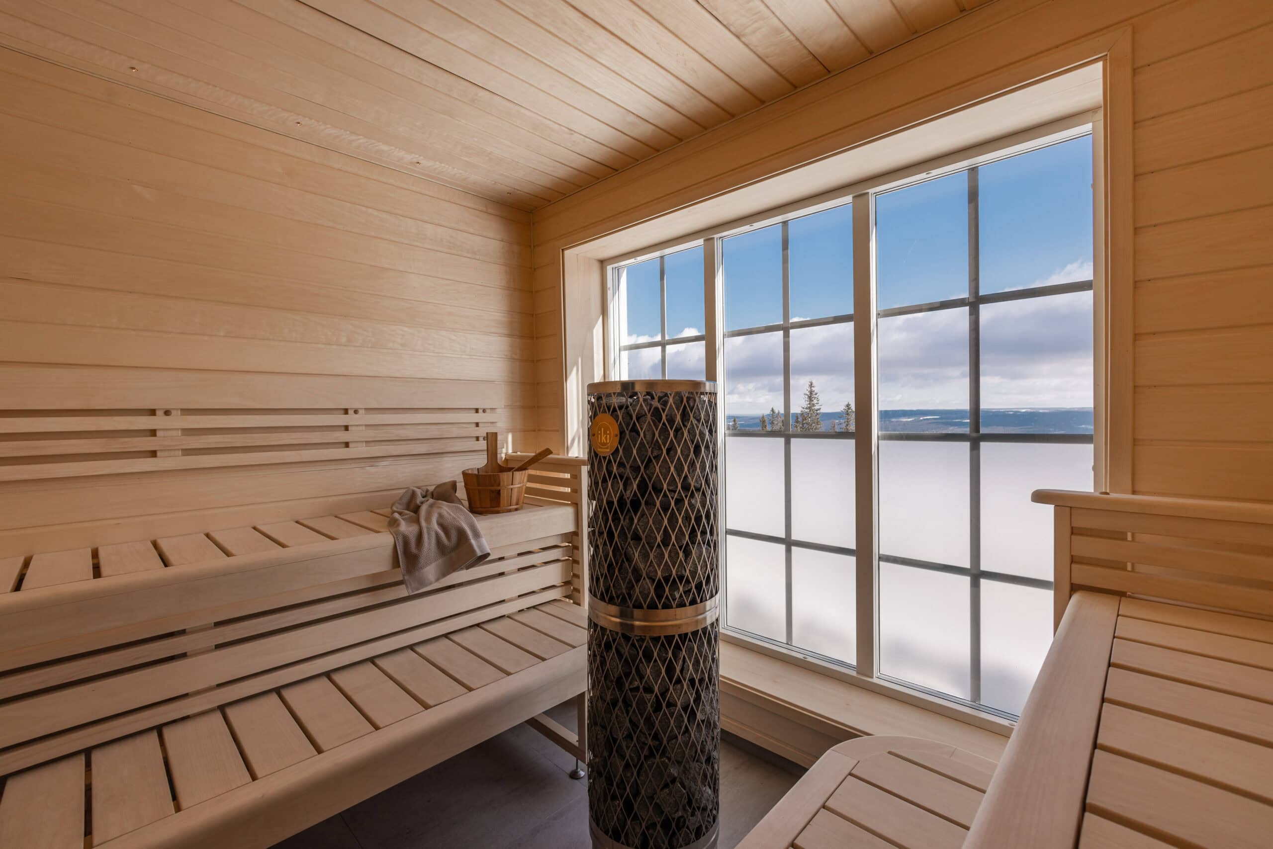 Vacker bastu inuti med träväggar och stor fönster som visar utsikt över vatten och himmel.