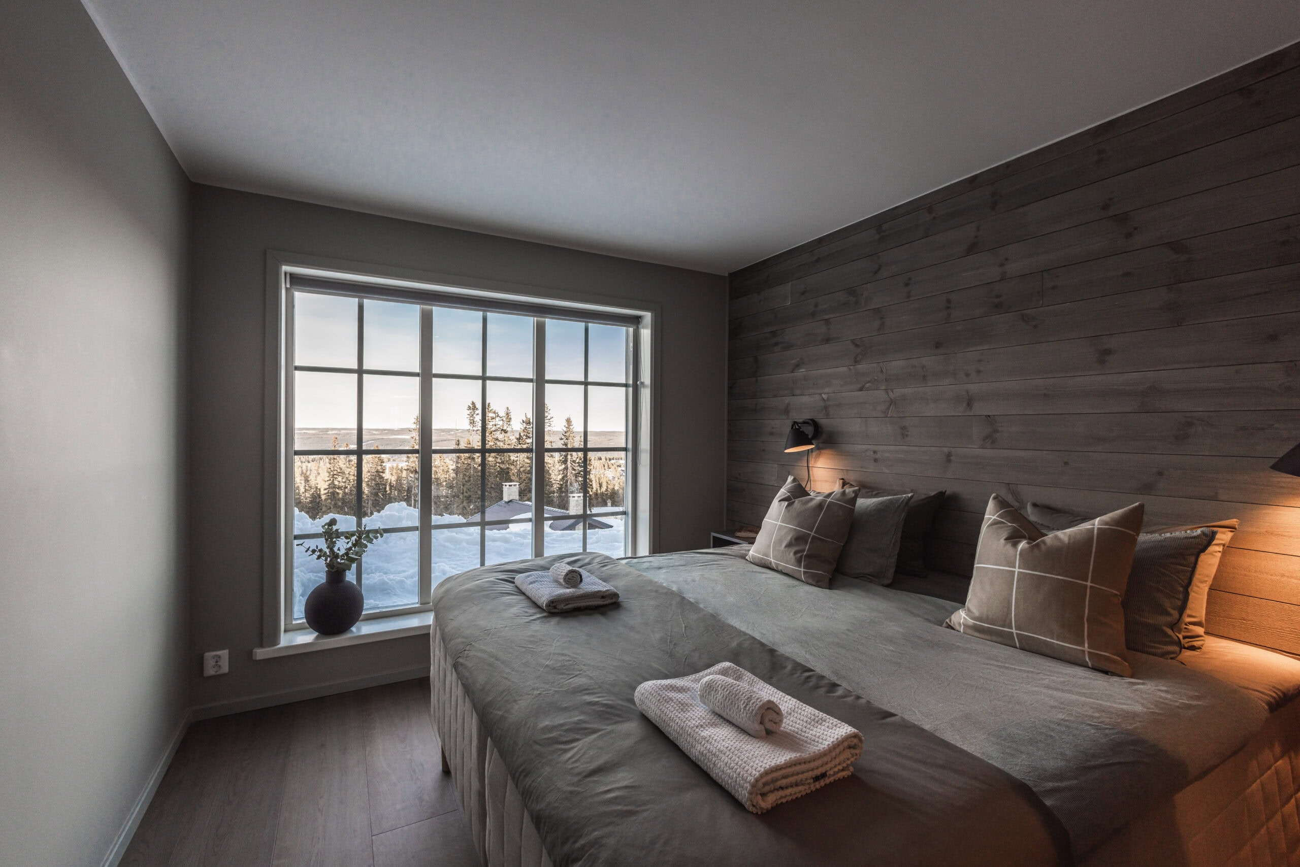 Ein gut ausgestattetes Schlafzimmer mit großen Fenstern, die den Blick auf die verschneite Landschaft draußen freigeben, moderner Einrichtung und einer gemütlichen Atmosphäre.