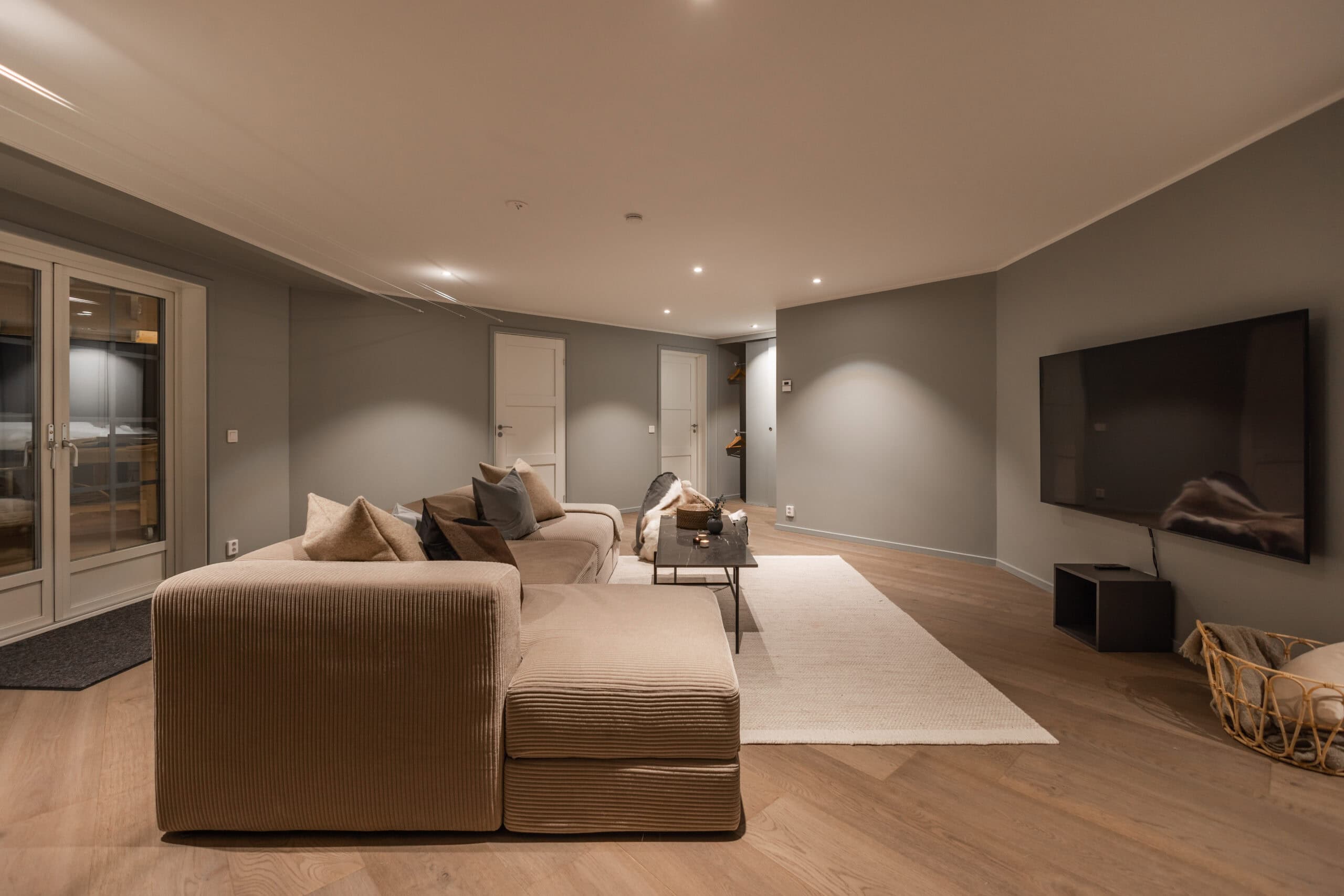 Modern living room with beige sofa, flat-screen TV, and wooden flooring, creating a cozy and stylish atmosphere.