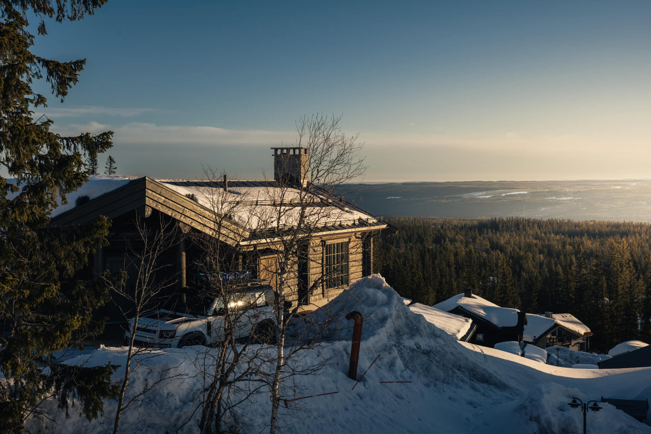 Salengodset, eine gemütliche Hütte in der verschneiten Landschaft mit Blick auf den Wald und die Berge im Hintergrund unter einem klaren Winterhimmel.