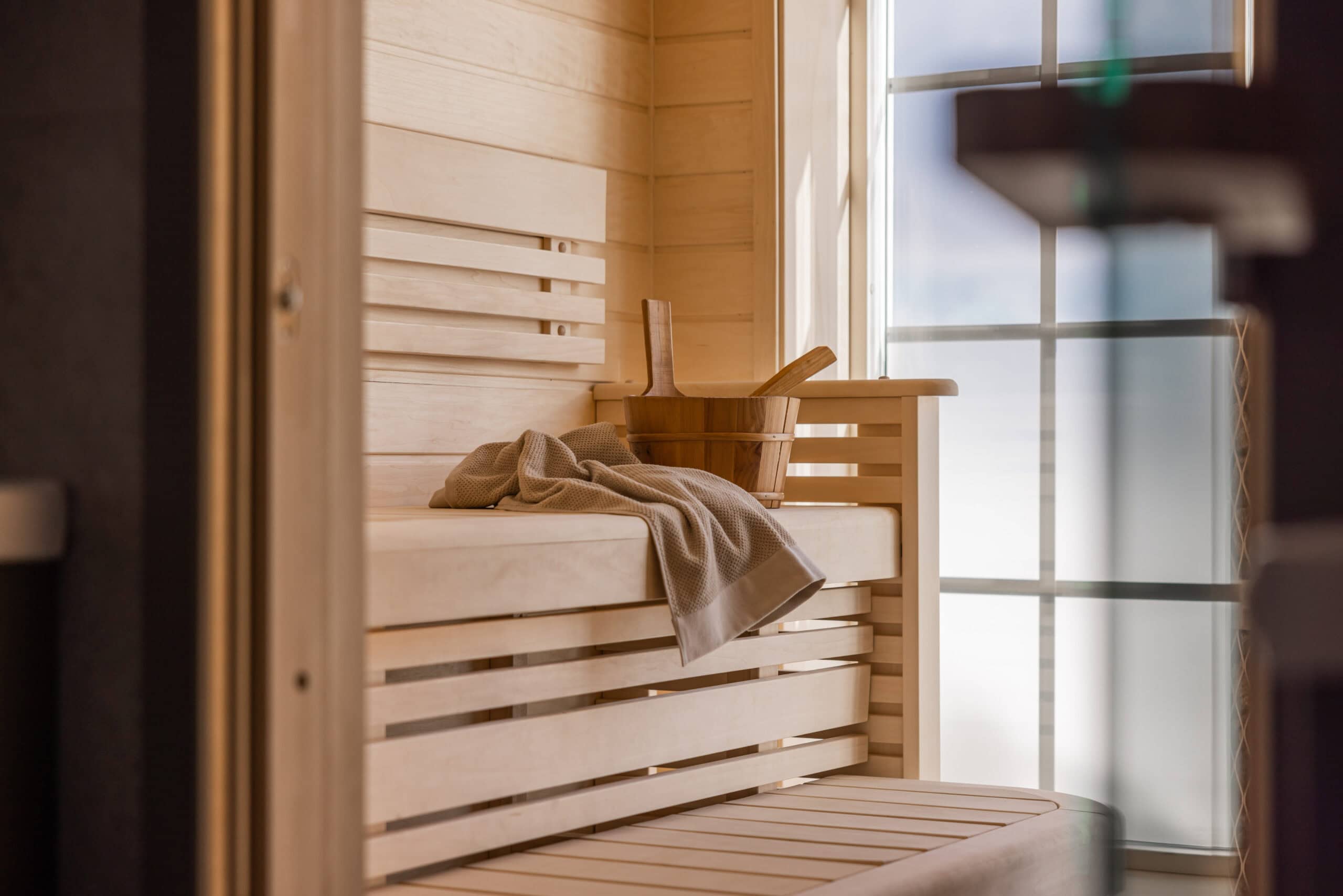 Modern bastu med träpaneler, sittbänk och stora fönster för naturligt ljus, perfekt för avkoppling och hälsa.