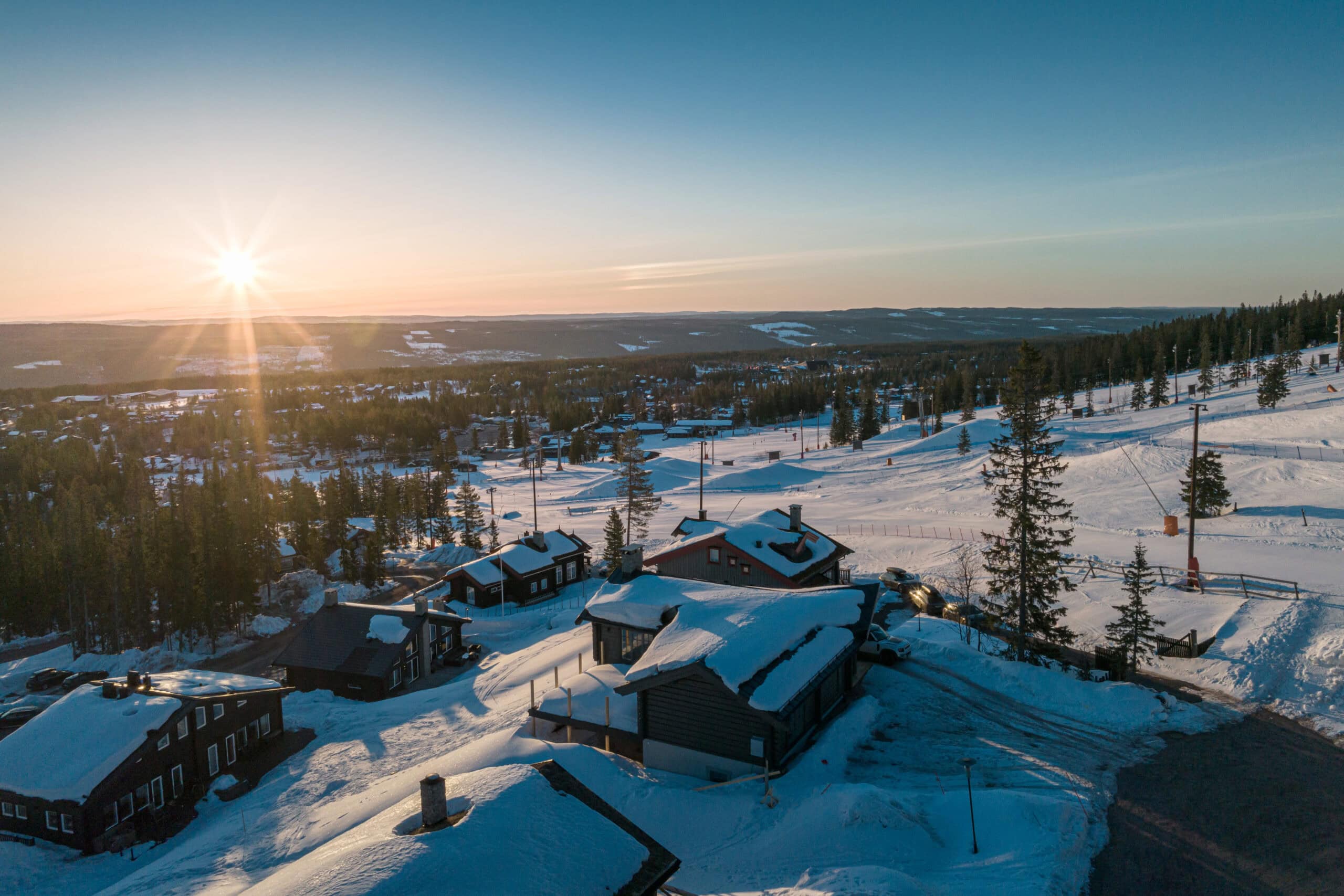 Snötäckta stugor i Salengodset med solnedgång i bakgrunden, vinterlandskap, träd och öppna fält.