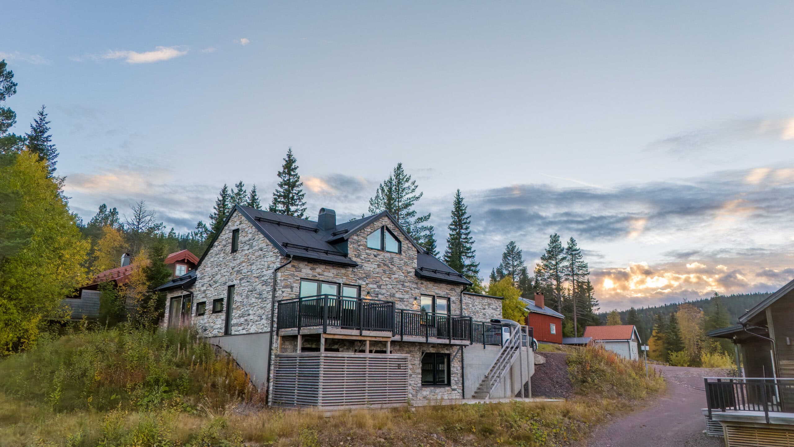 An exterior view of Stenlodgen in the autumn light, with its façade of natural stone and wood, surrounded by the forest.