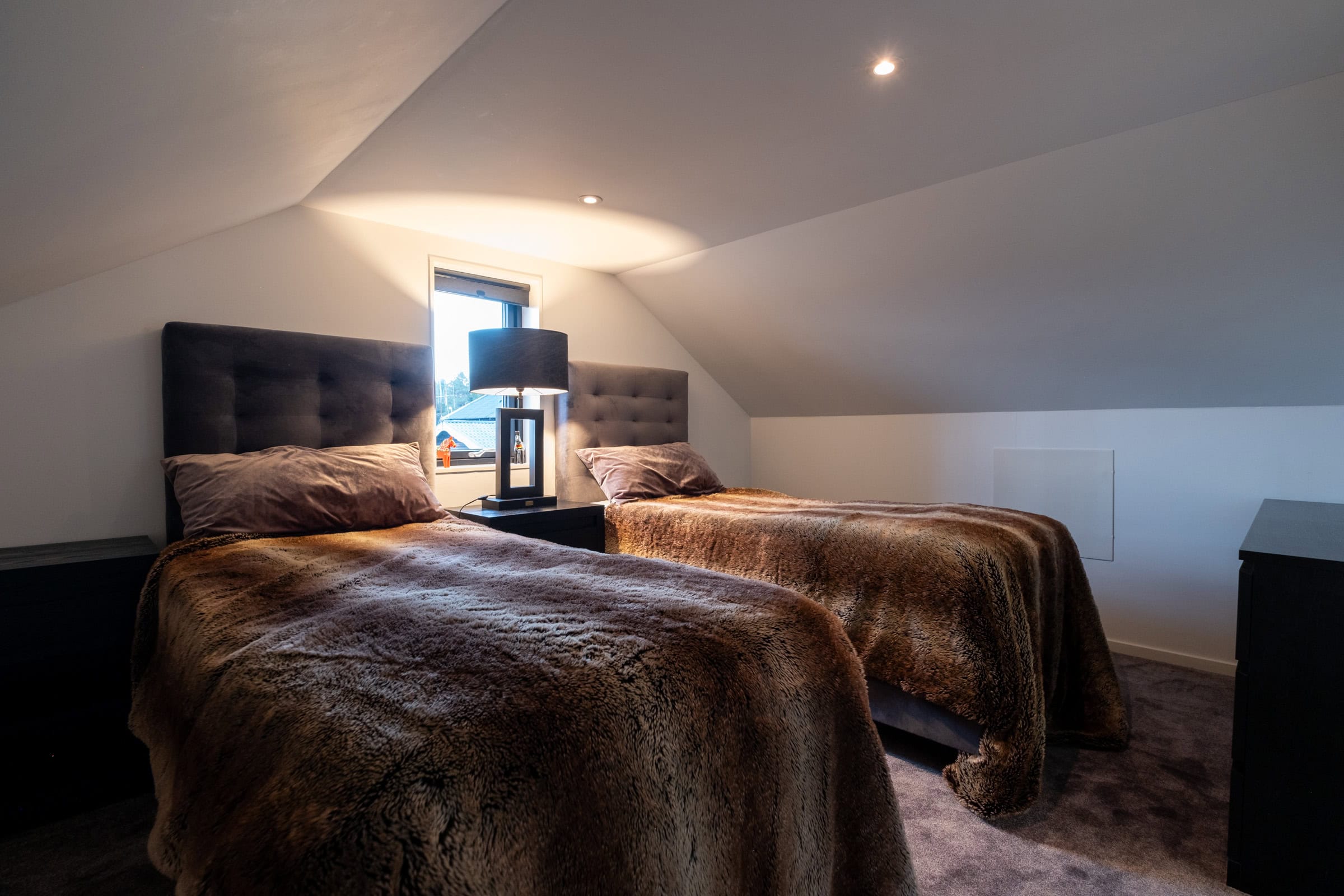 A bedroom in the loft with two single beds and a bedside table between them.