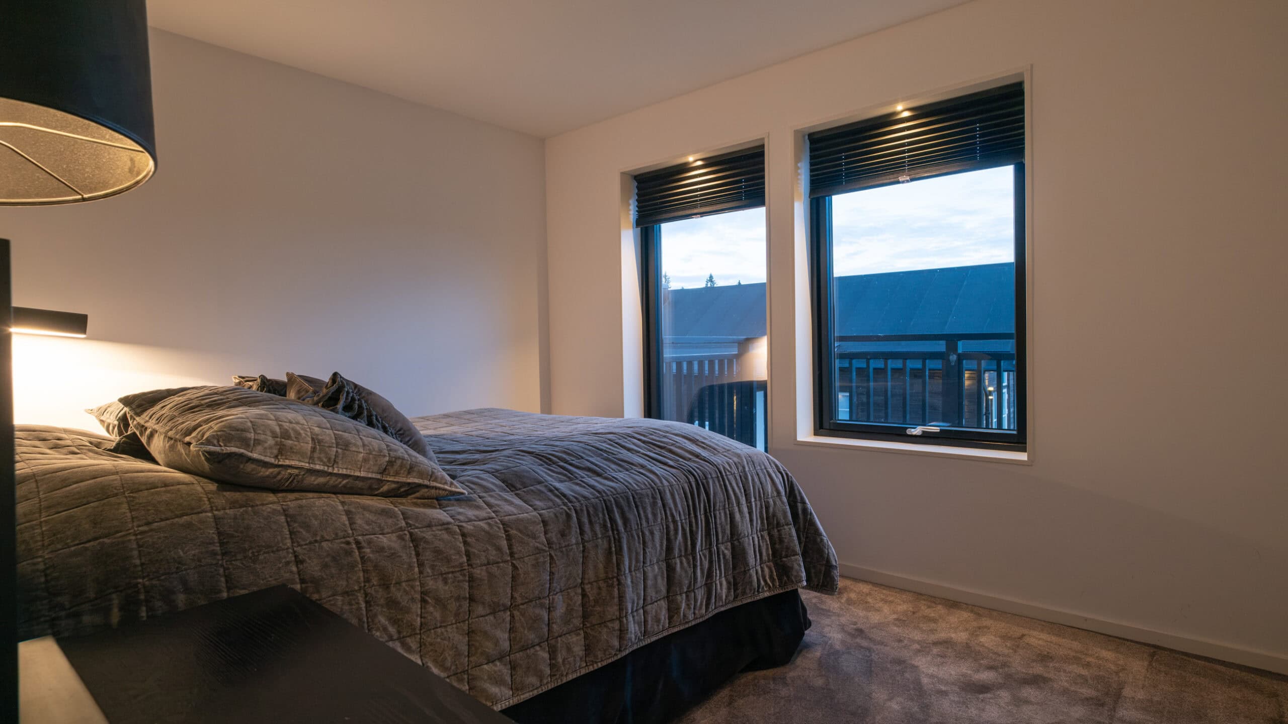 Bedroom with a double bed, a reading lamp and two windows.