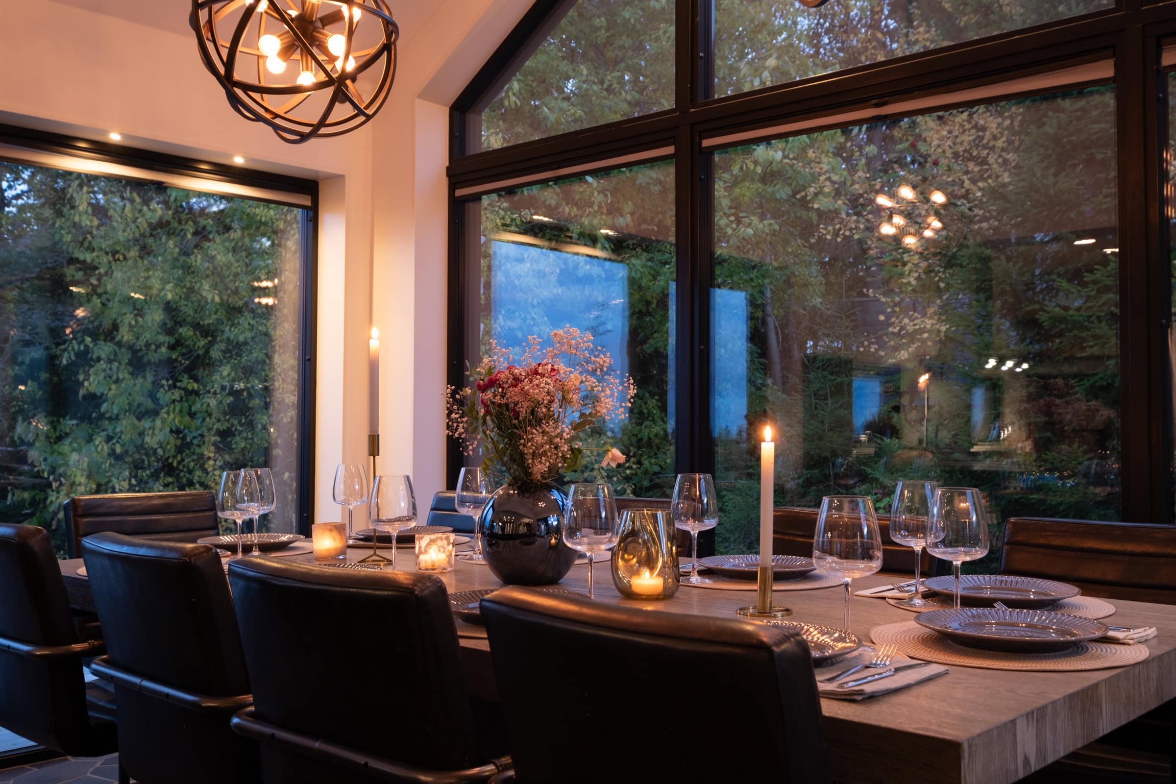 A table laid with candles and flowers in front of the window wall.