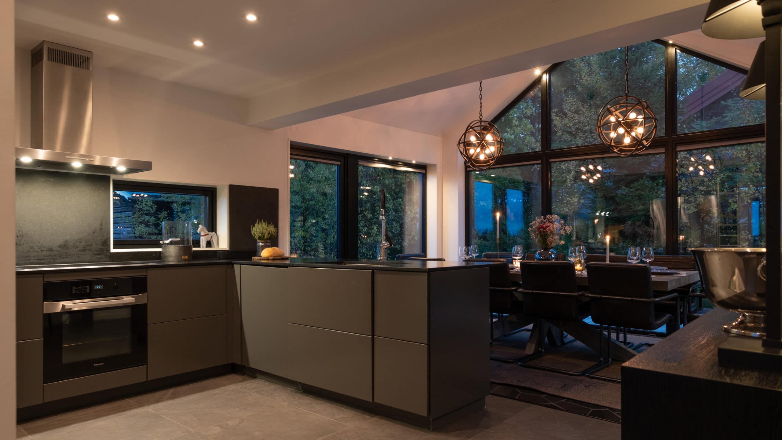 The kitchen in the evening light, with the dining area and the end wall of windows behind it.