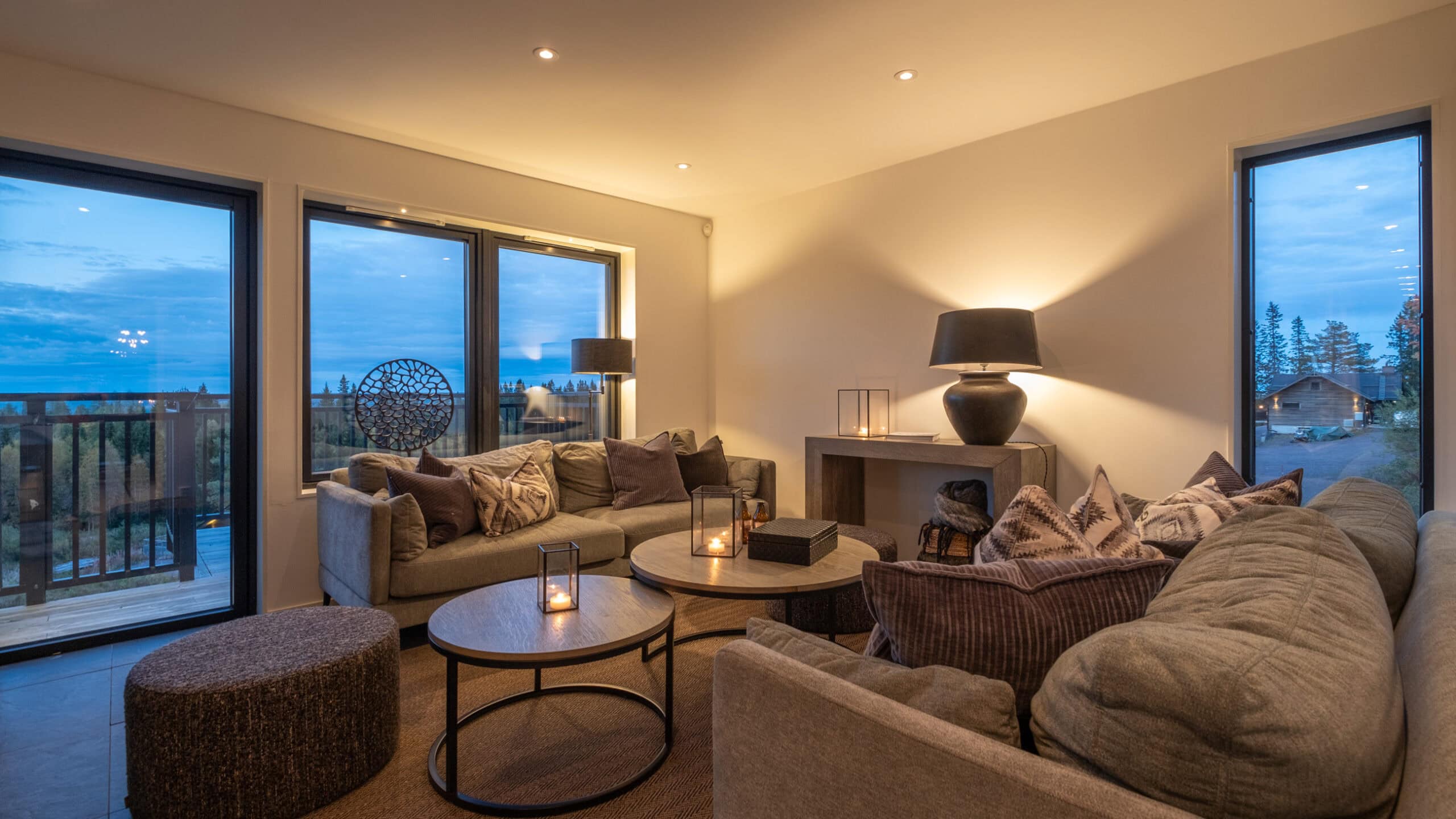 The living room at dusk, with a sofa, pouffes and a window leading onto the balcony.
