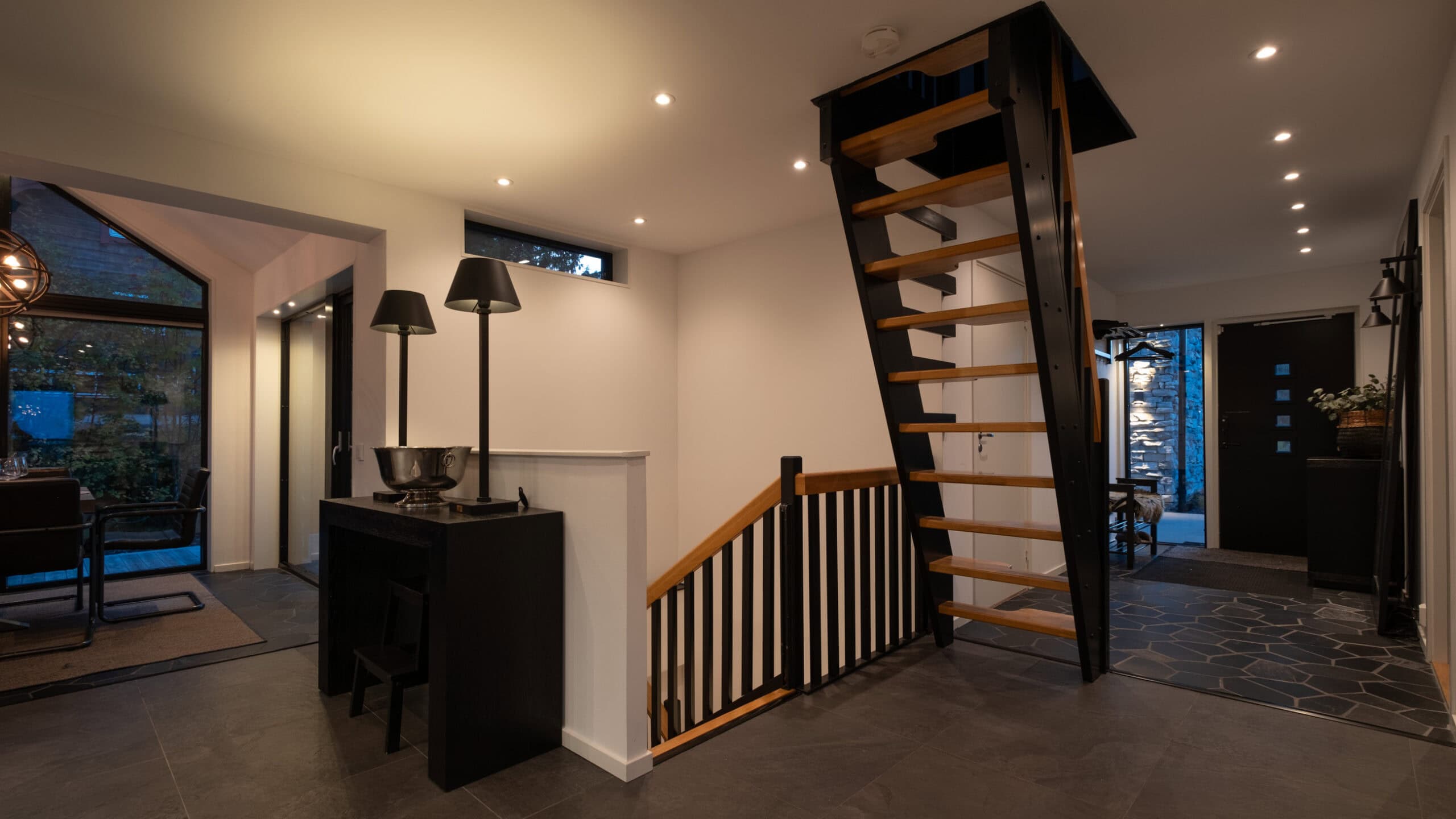The hall with an open wooden staircase leading up to the loft and the front door next to it.