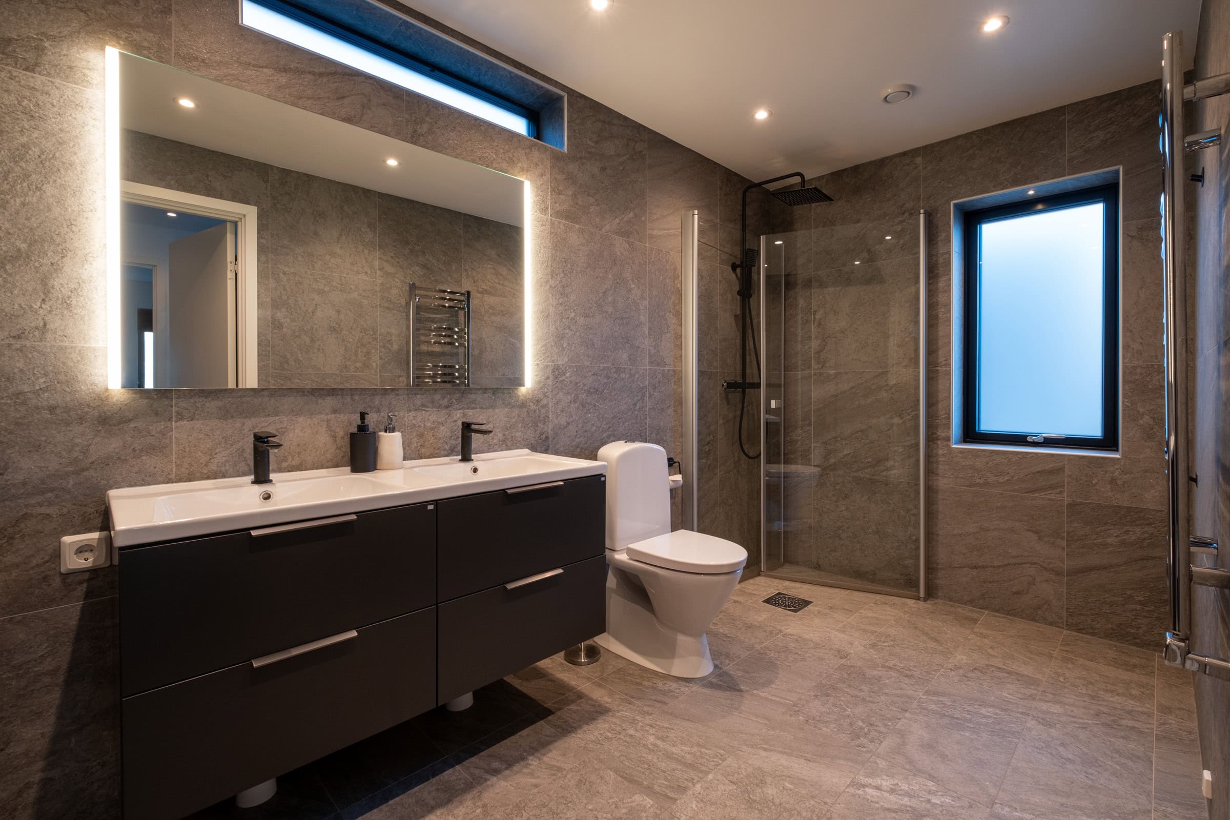 Bathroom with twin washbasins, a lighted mirror, a glass-enclosed shower and a heated towel rail.