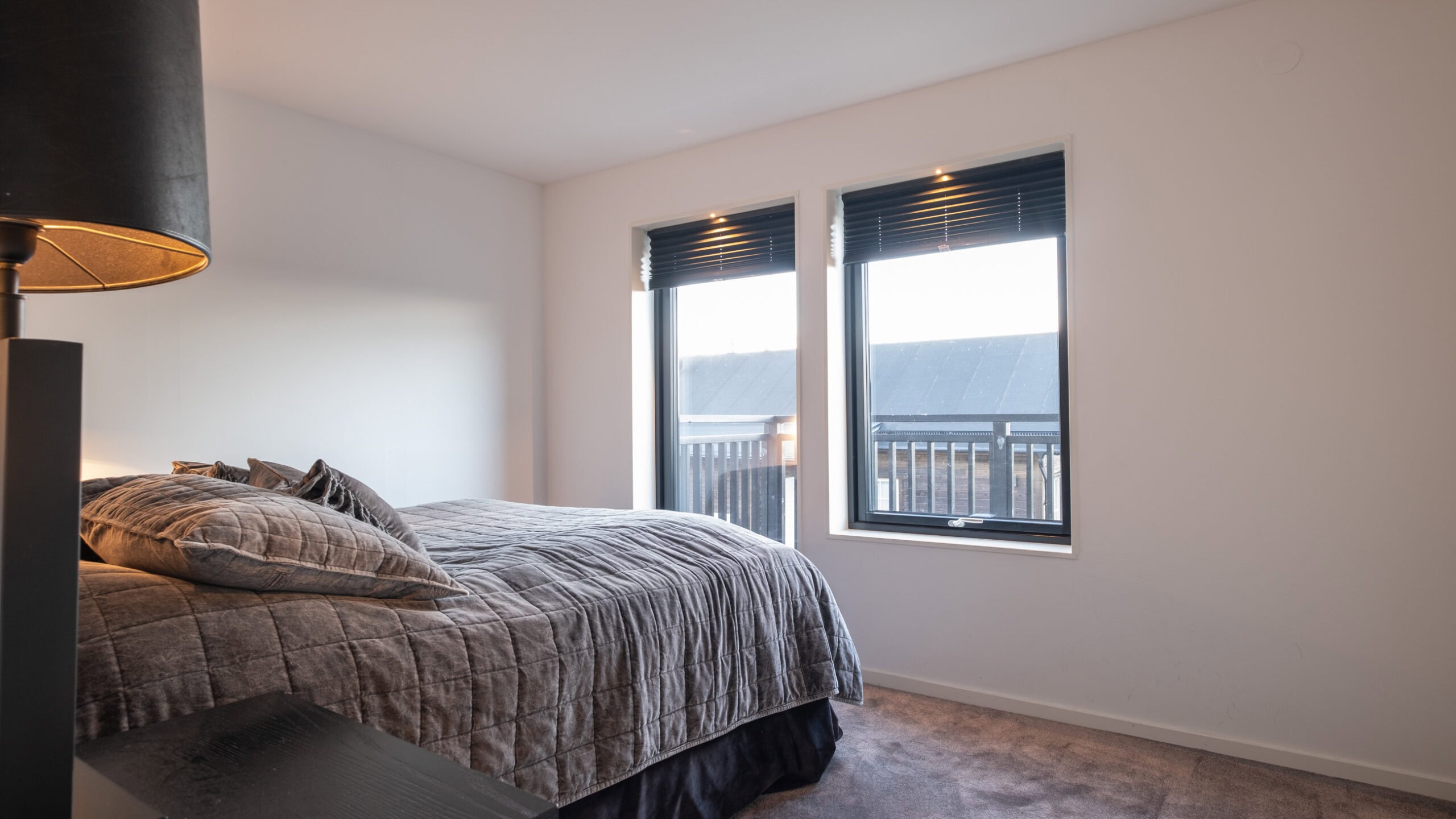 A bedroom with a double bed and two windows overlooking the balcony.