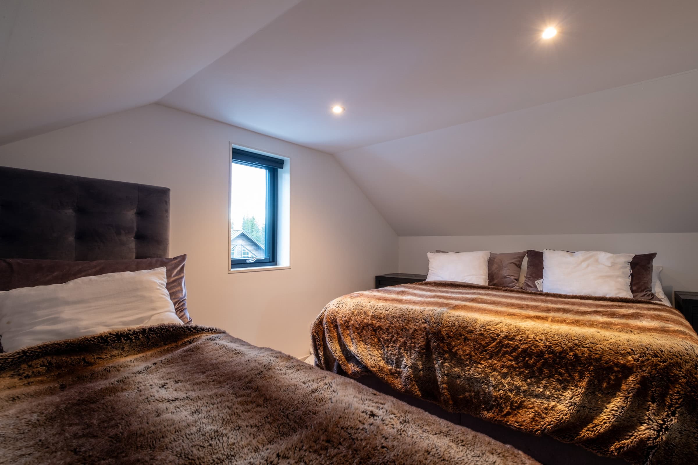 A bedroom with a sloping ceiling, featuring a double bed and a fold-down bed above it.