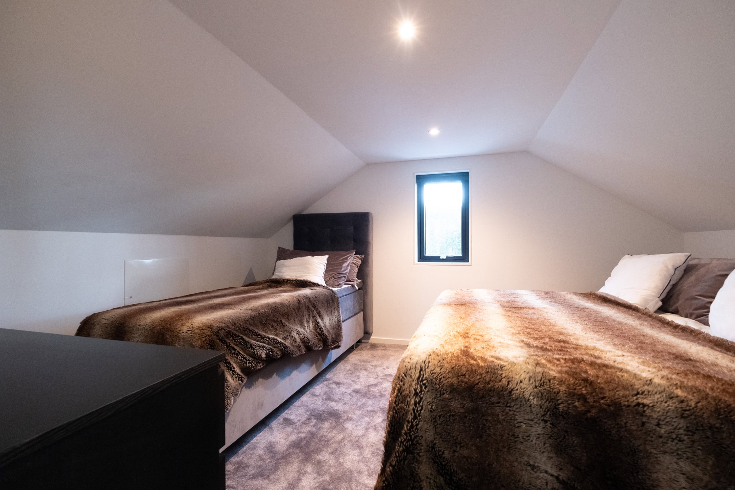 A bedroom with a sloping ceiling, featuring two single beds and folding beds.