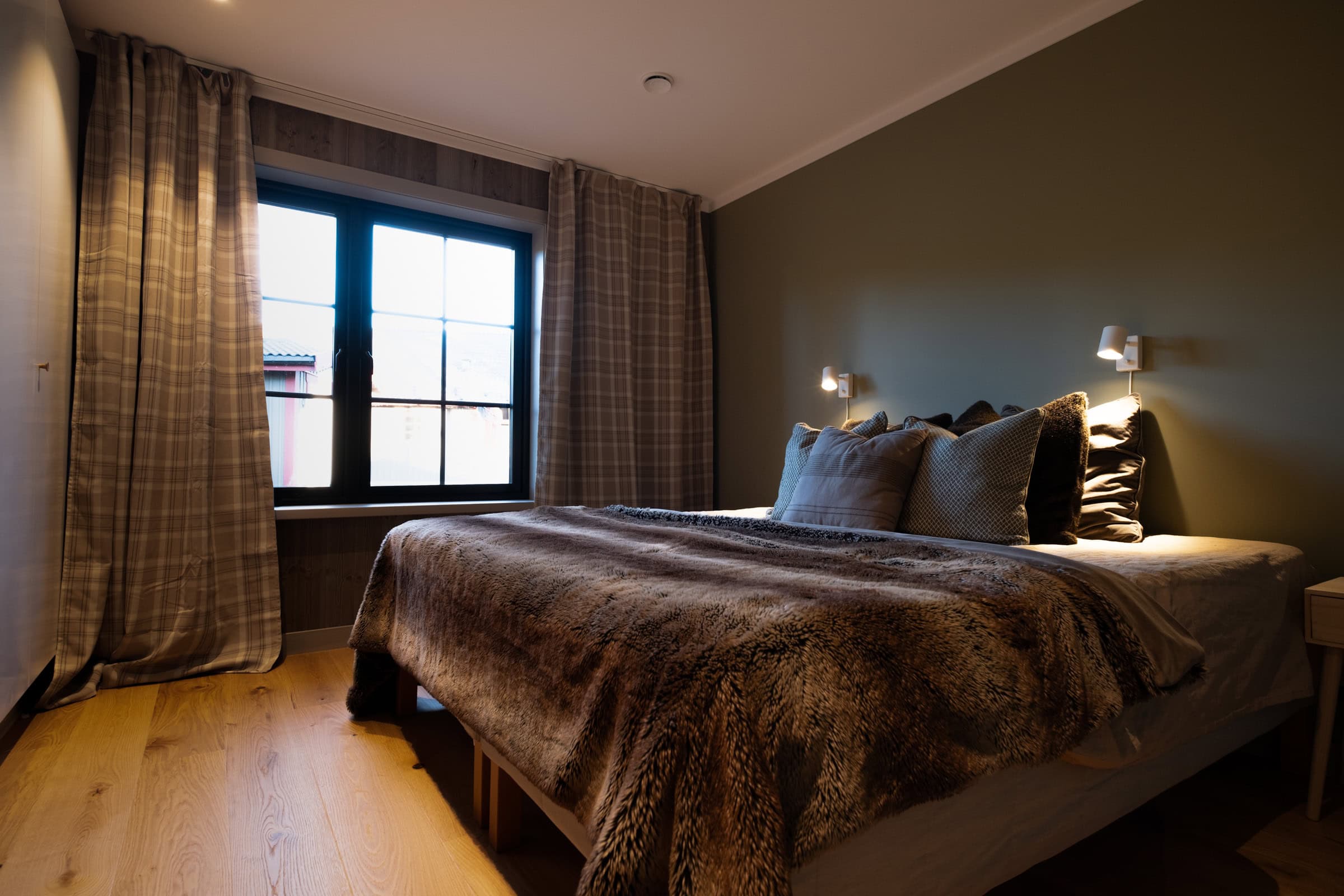 Bedroom with a double bed, chequered curtains and a dark green feature wall