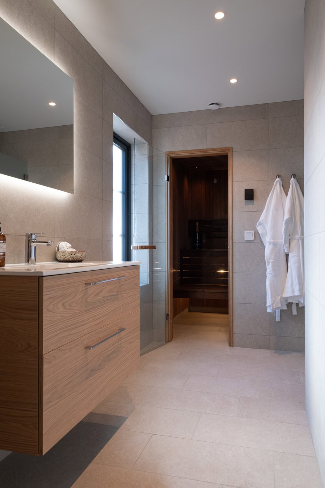Bathroom with an oak washbasin, a mirror with lighting and a door to the sauna