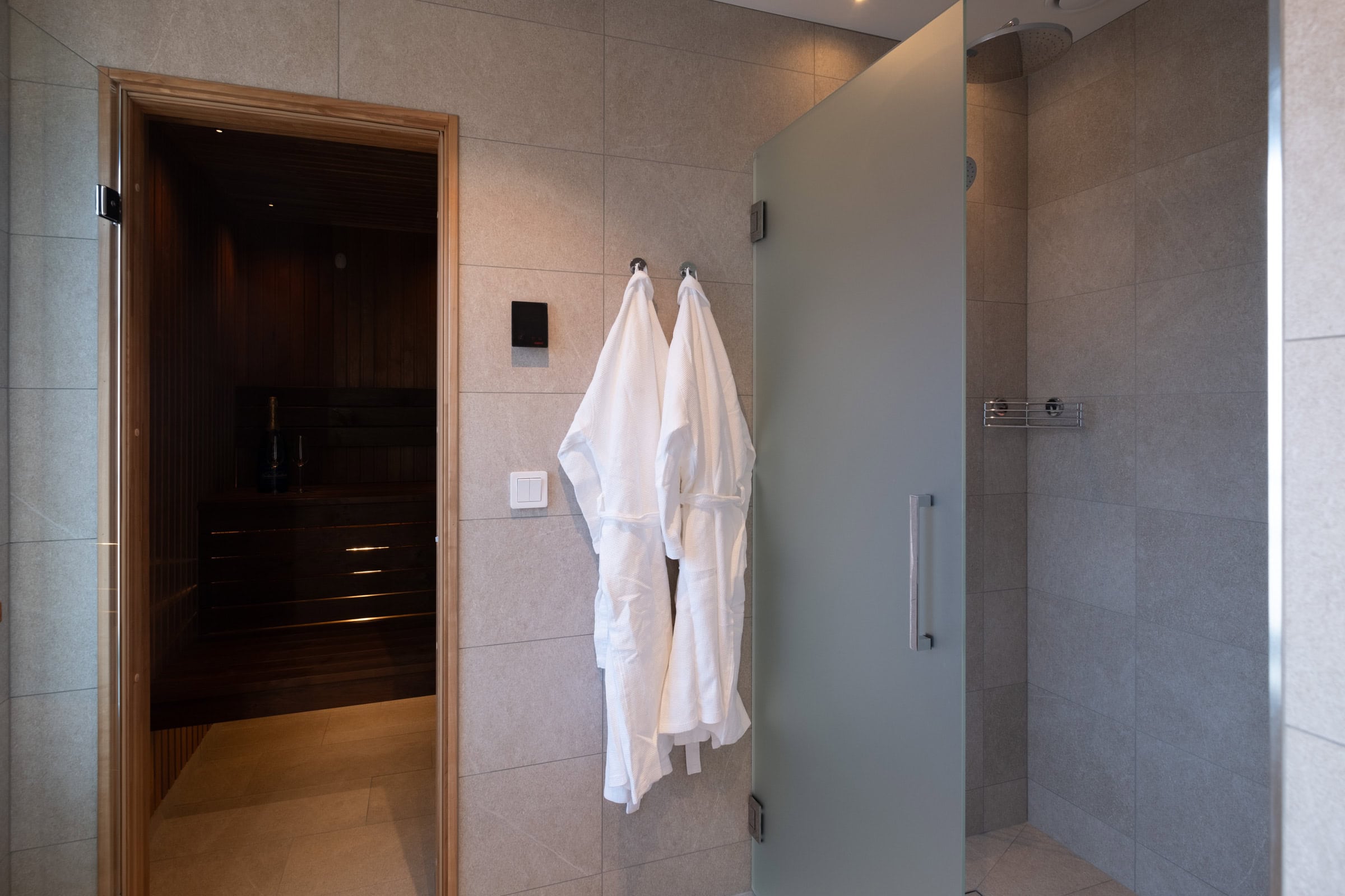 Entrance to the sauna with a bathrobe and a glass door leading to the shower