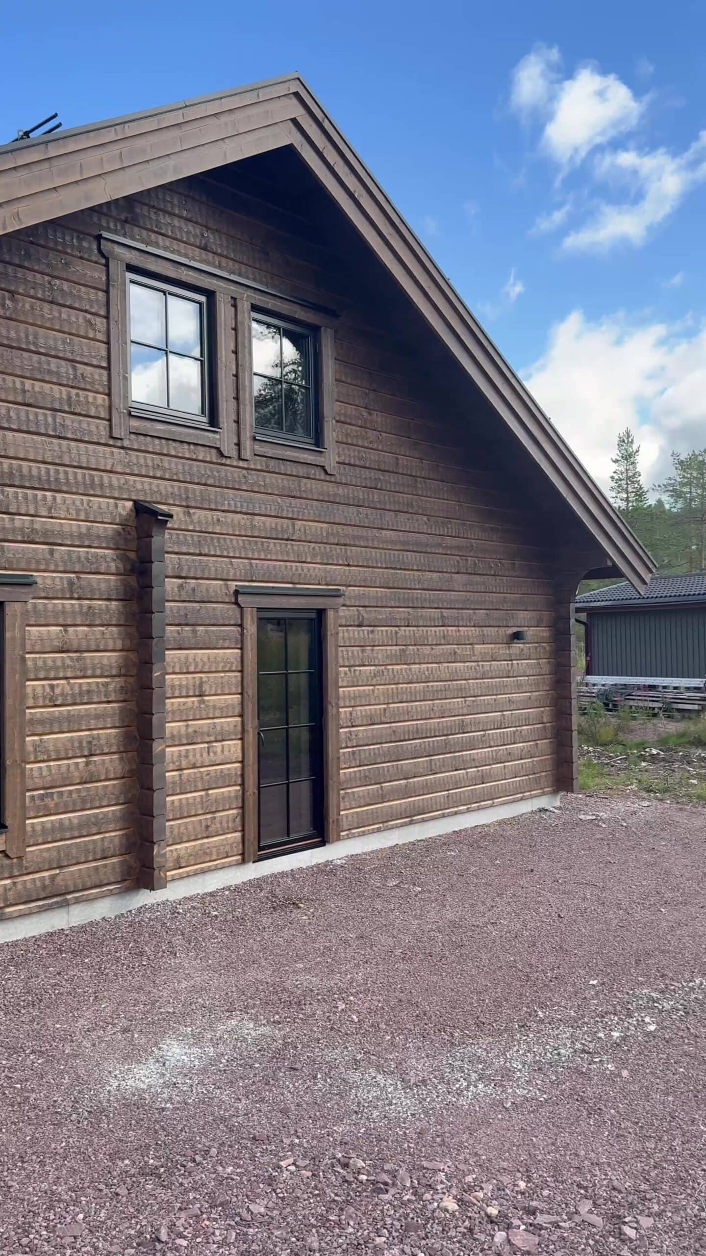 Die Längsseite der Villa Åsstigen mit dunkelbrauner Holzvertäfelung, der Eingangstür und den Fenstern im Obergeschoss, im Hintergrund das Gästehaus.